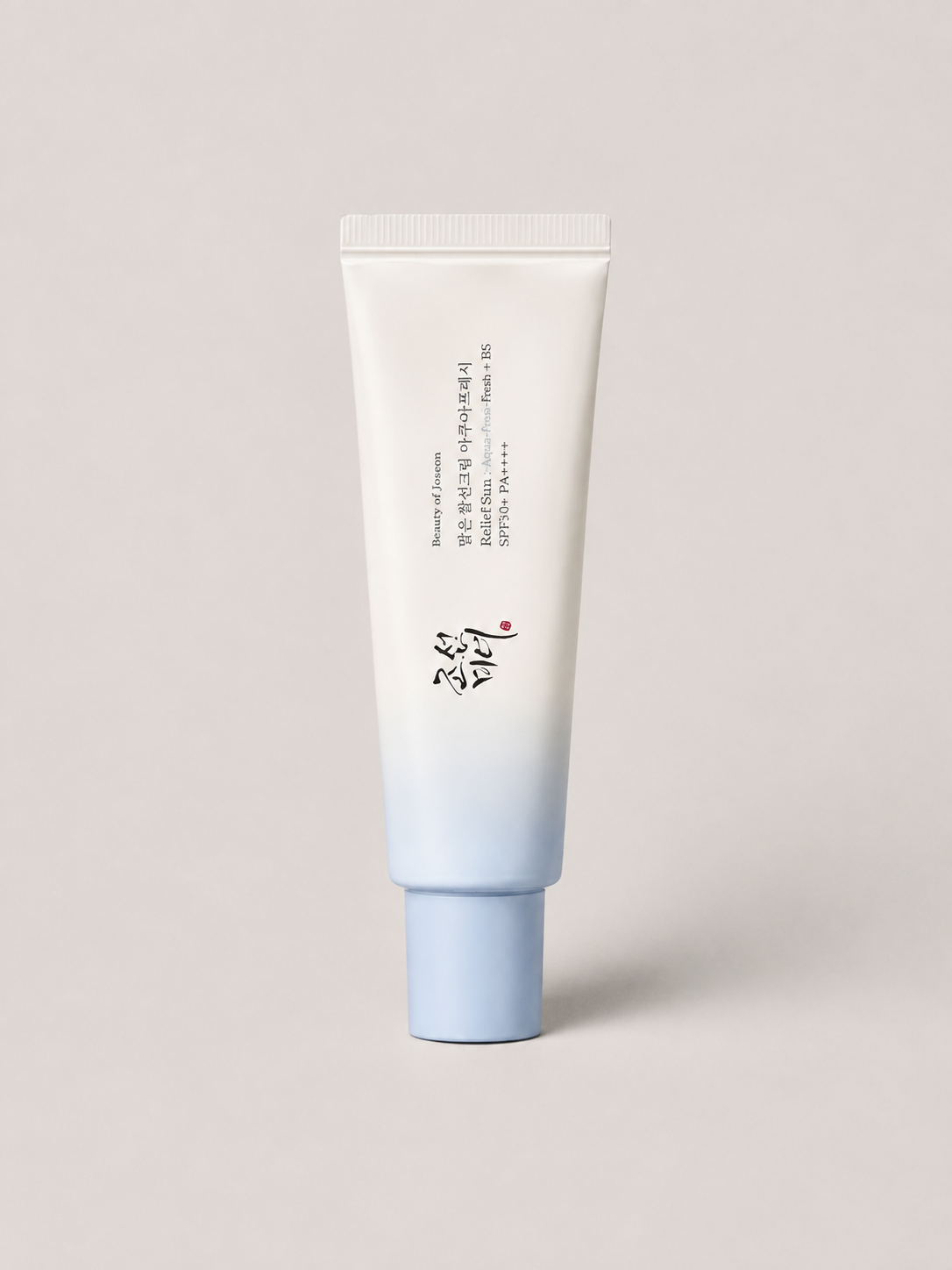 A korean skincare SPF cream tube with a white to light blue gradient design, standing upright against a neutral light gray background. The tube features Beauty of Joseon Relief Sun Aqua-Fresh: Rice + B5. SPF 50+, 50 ml.
