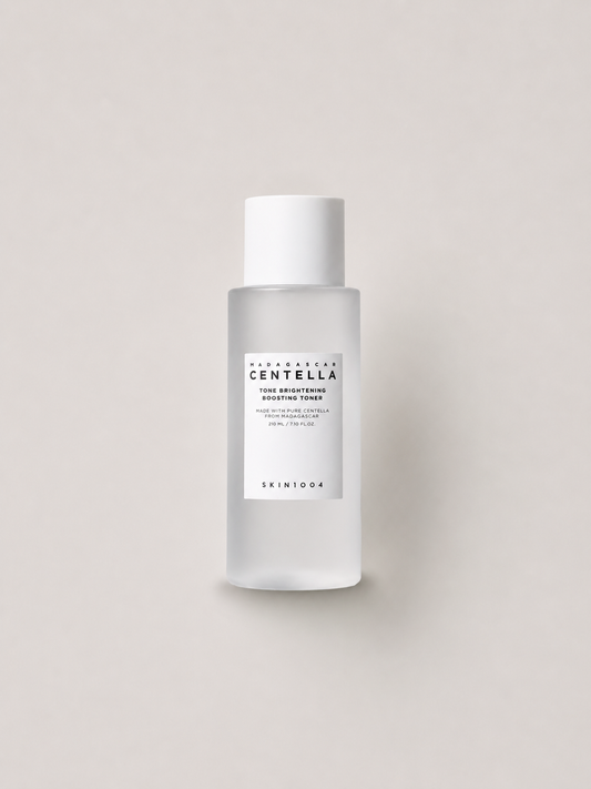 A bottle of Korean skincare toner -  SKIN1004 Madagascar Centella Tone brightening Boosting Toner, featuring a frosted glass bottle and a white cap, set against a solid light beige background. 210 ml.
